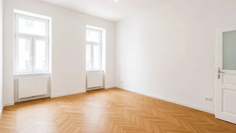 Helles, leeres Zimmer mit Fischgrätparkett und zwei großen Fenstern, bereit zur individuellen Gestaltung.