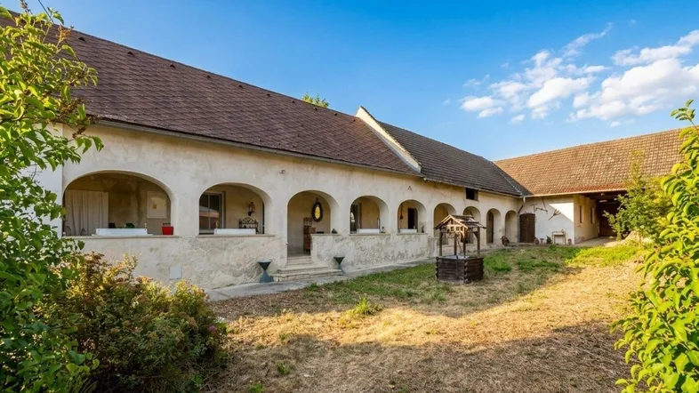 Innenhof des Anwesens mit Arkadengang und einem alten Brunnen, umgeben von Natur.