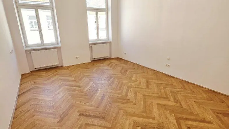 Leeres Zimmer mit elegantem Fischgrätparkett und hellen Wänden, bereit zur individuellen Gestaltung.