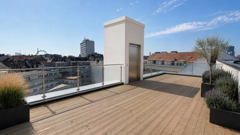 Geräumige Dachterrasse mit Holzboden, Glasgeländer und Panoramablick über die Stadt. Ein Aufzug ist ebenfalls sichtbar.