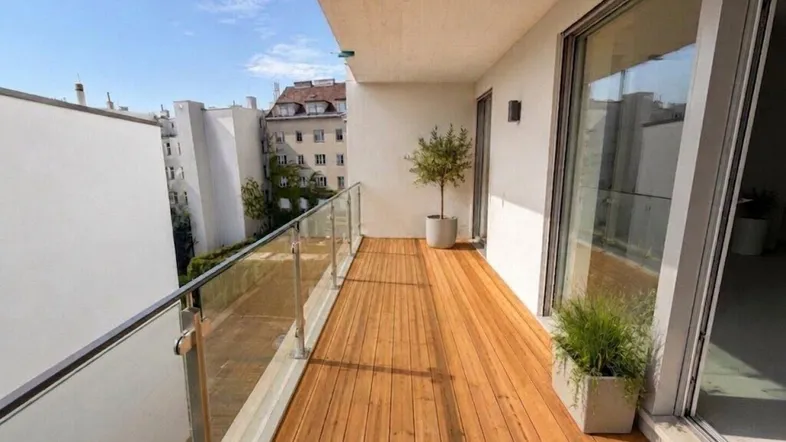 Moderner Balkon mit Holzfußboden, Glasgeländer und Blick auf die umliegenden Gebäude.