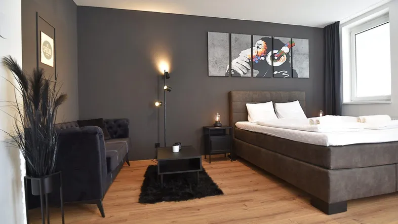 Modernes Schlafzimmer mit dunklen Wänden, Holzboden und einem großen Bett sowie einer gemütlichen Sitzecke.