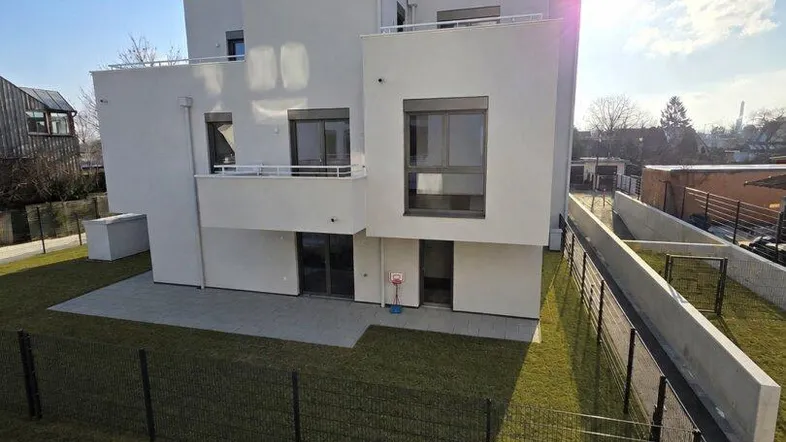 Modernes weißes Mehrfamilienhaus mit gestufter Architektur und Grünflächen im Vordergrund unter strahlendem Himmel.