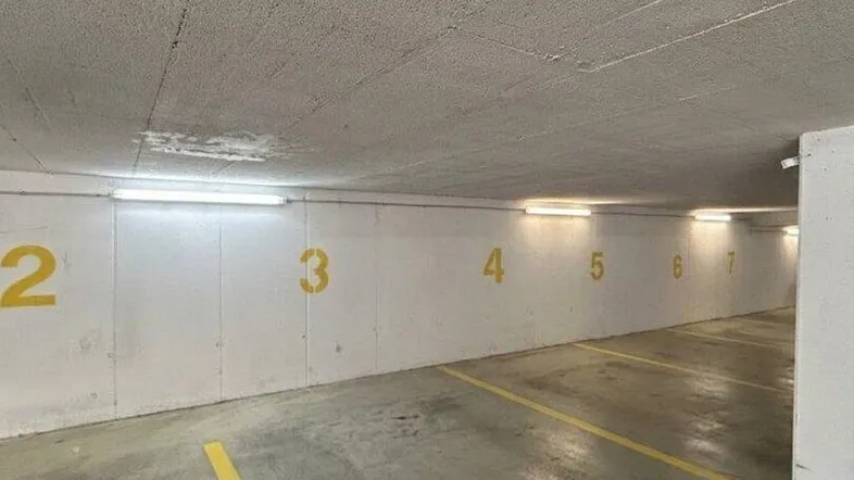Geräumige Tiefgarage mit nummerierten Stellplätzen, Betonboden und Leuchtstoffröhrenbeleuchtung.