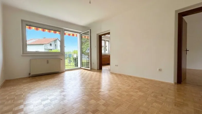 Helles Wohnzimmer mit Parkettboden und Zugang zu einem Balkon oder Gartenbereich.