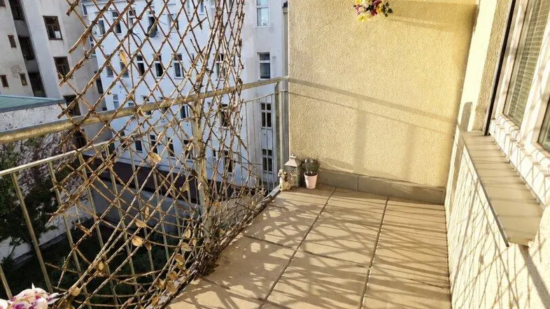 Heller Balkon mit Fliesenboden und Blick auf die umliegenden Gebäude, teilweise beschattet von einer Markise.