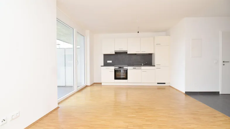 Heller offener Wohn-Essbereich mit integrierter Küche, Parkettboden und Zugang zum Balkon.