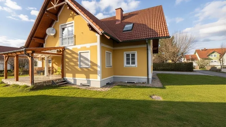 Gelbes Einfamilienhaus mit rotem Ziegeldach, gepflegtem Rasen und überdachter Terrasse.