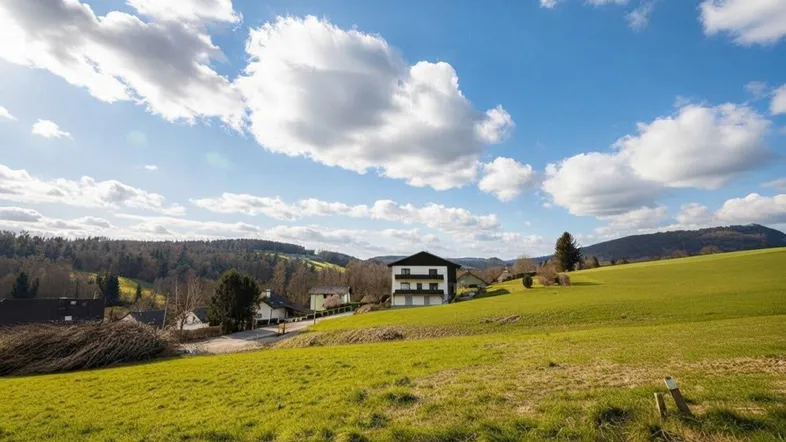 Modernes Gebäude in ländlicher Umgebung mit weiten grünen Feldern und Hügeln im Hintergrund.