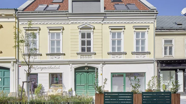 Historische Gebäudefassade mit Dachfenstern und Geschäften im Erdgeschoss unter blauem Himmel.