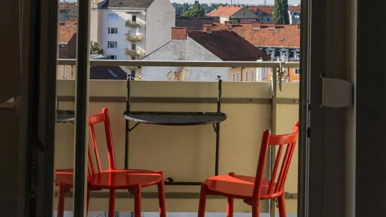 Gemütlicher Balkon mit rotem Mobiliar und Blick über die Stadt.