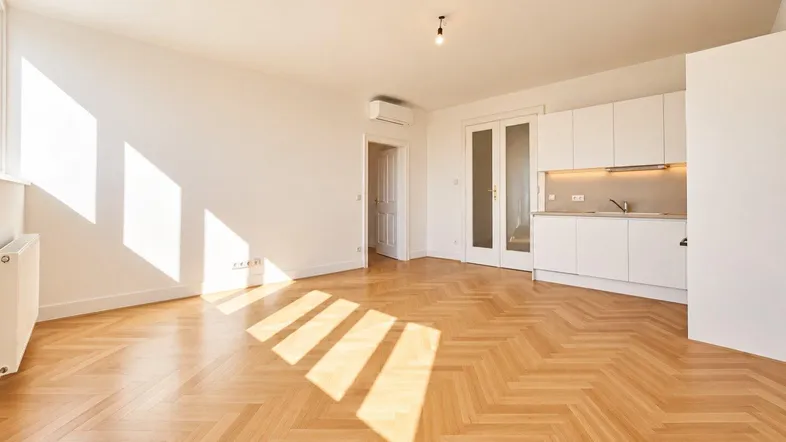 Helles Wohnzimmer mit Fischgrätparkett, integrierter Küchenzeile und viel natürlichem Licht.