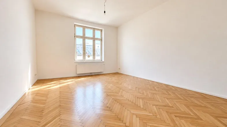 Helles Zimmer mit Fischgrätparkett und großem Fenster, ideal als Wohn- oder Schlafzimmer.
