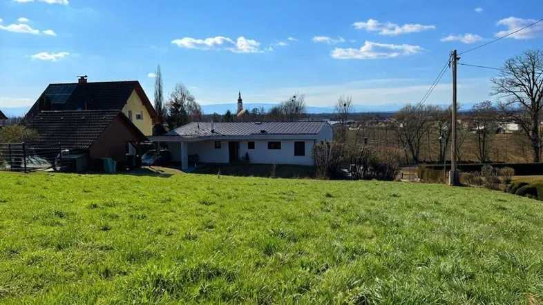 Weitläufige grüne Wiese mit Blick auf umliegende Häuser und die ländliche Umgebung unter blauem Himmel.