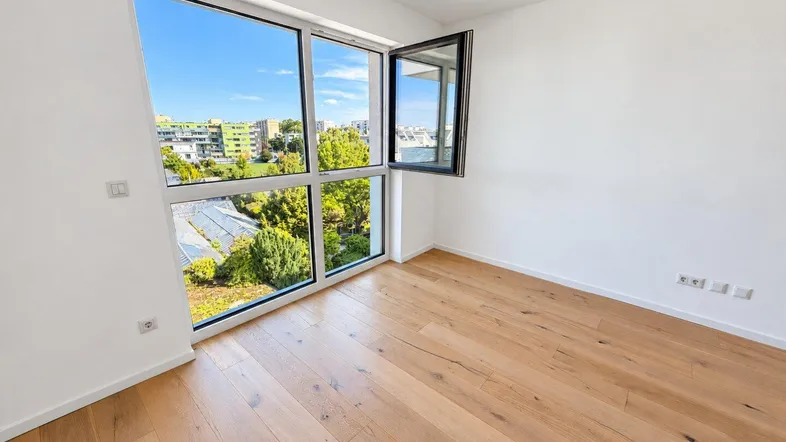 Helles Zimmer mit großen Fenstern, Holzboden und Blick ins Grüne, ideal als Schlafzimmer.