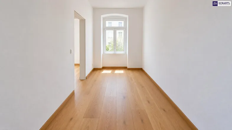 Helles, leeres Zimmer mit Holzboden und einem Fenster, das viel Tageslicht hereinlässt.