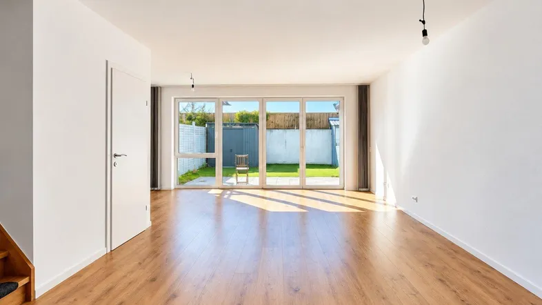 Helles Wohnzimmer mit Laminatboden und Zugang zu einer kleinen Terrasse und Garten.