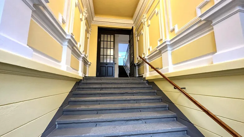 Repräsentatives Treppenhaus mit Stuckverzierungen und gelben Wänden, das den Eingangsbereich des Gebäudes zeigt.