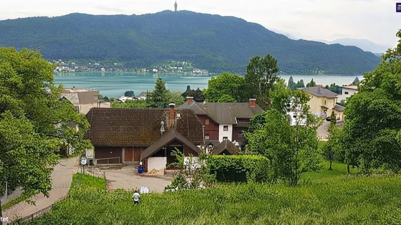 Panoramablick auf den Wörthersee mit umliegenden Häusern und grünen Bergen im Hintergrund.
