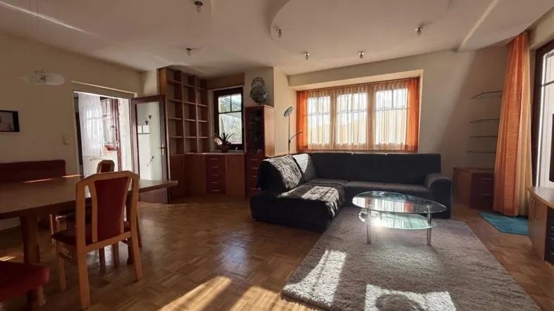 Helles Wohn- und Esszimmer mit Parkettboden, gemütlicher Sitzecke und integrierten Regalen.