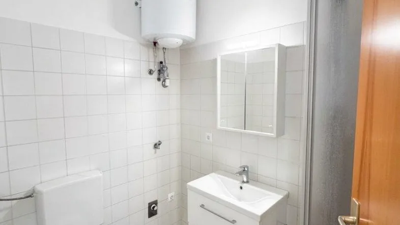 Helles Badezimmer mit Dusche, WC, Waschbecken und einem Warmwasserboiler an der Wand.