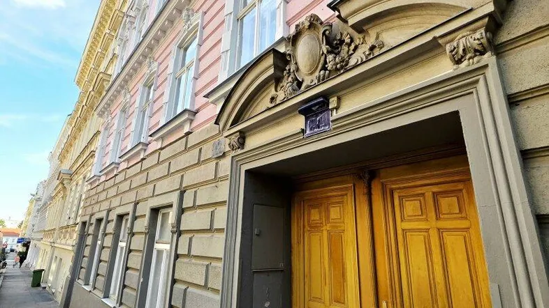 Historisches Gebäude mit rosafarbener Fassade und einer großen, verzierten Holztür an der Straße.