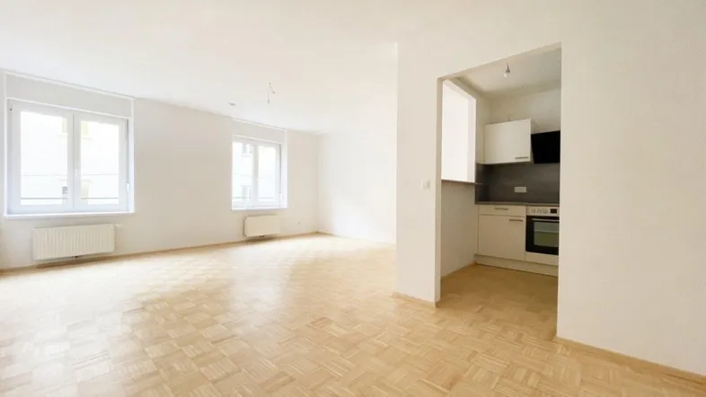 Helles Wohnzimmer mit Parkettboden und großen Fenstern, offen zu einer Küchenzeile.