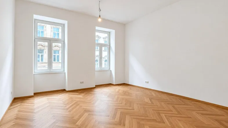 Helles, leeres Zimmer mit Fischgrätparkett und zwei großen Fenstern, bereit zur individuellen Gestaltung.