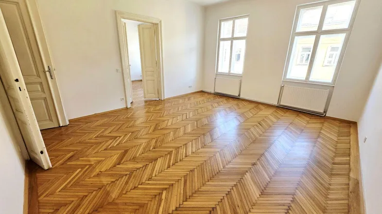 Helles Zimmer mit Fischgrätparkettboden und hohen Fenstern, bereit zur individuellen Gestaltung.