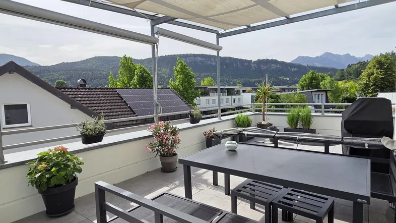 Geräumige Dachterrasse mit Essbereich, Grill und weitreichendem Bergblick unter einer Pergola.