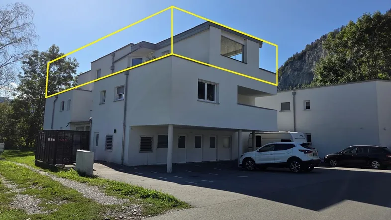 Modernes Mehrfamilienhaus mit weißer Fassade und Flachdach, umgeben von Natur und Bergen.