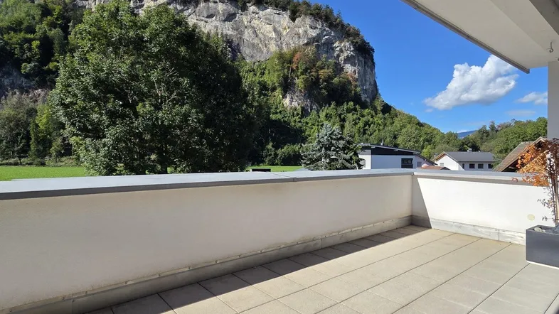 Geräumige Terrasse mit Fliesenboden und beeindruckendem Blick auf die umliegende Berglandschaft und grüne Wiesen.
