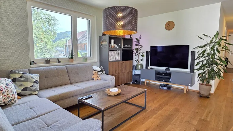 Helles Wohnzimmer mit beigem Ecksofa, Holzboden und Blick ins Grüne.