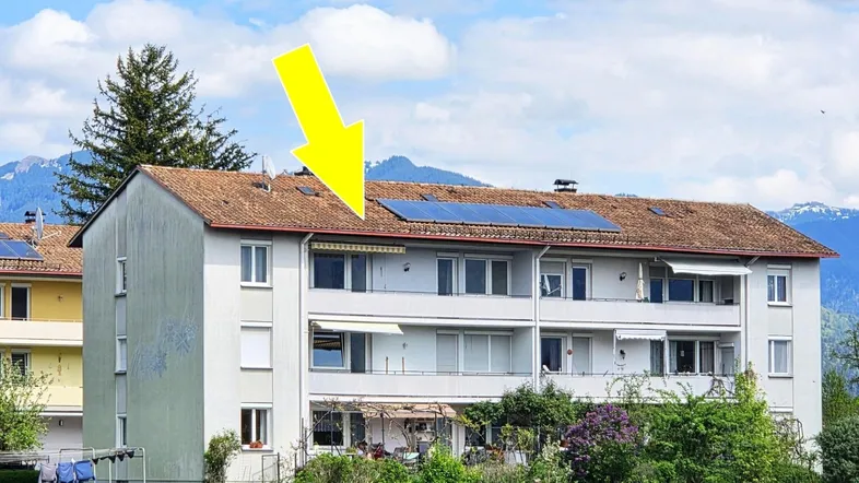 Mehrfamilienhaus mit Photovoltaikanlage auf dem Dach und Bergblick im Hintergrund.