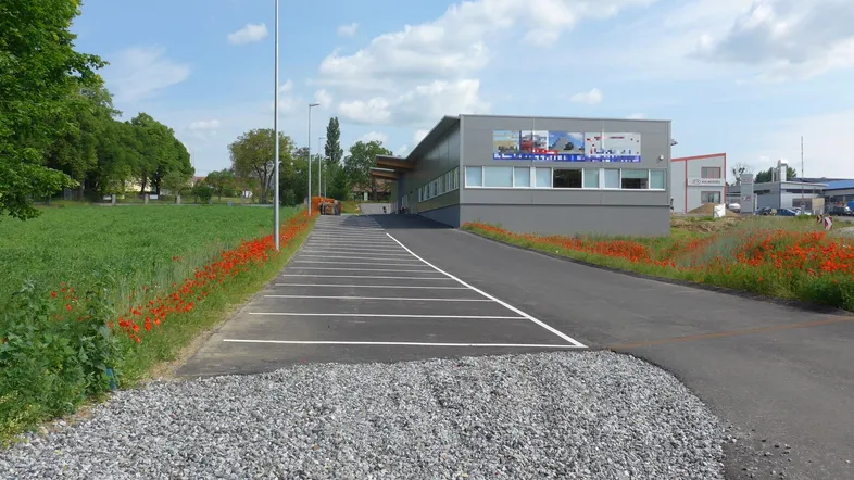 Modernes Geschäftsgebäude mit großem Parkplatz und angrenzendem Grünstreifen unter blauem Himmel.