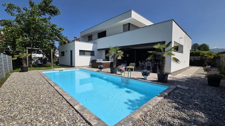 Modernes Haus mit klarem Design, umgeben von einem gepflegten Garten mit großem Swimmingpool.