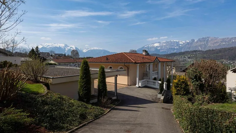 Großzügige Villa mit weitläufiger Auffahrt und beeindruckendem Bergblick unter blauem Himmel.