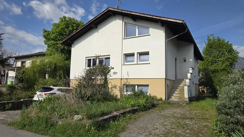Freistehendes Einfamilienhaus mit heller Fassade, Satteldach und einem Vorgartenbereich.