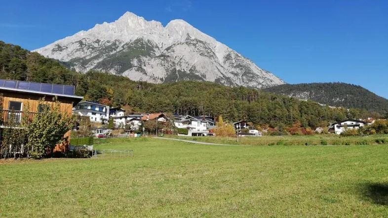 Weitläufiges grünes Feld mit Blick auf die majestätischen Berge und umliegende Häuser unter blauem Himmel.