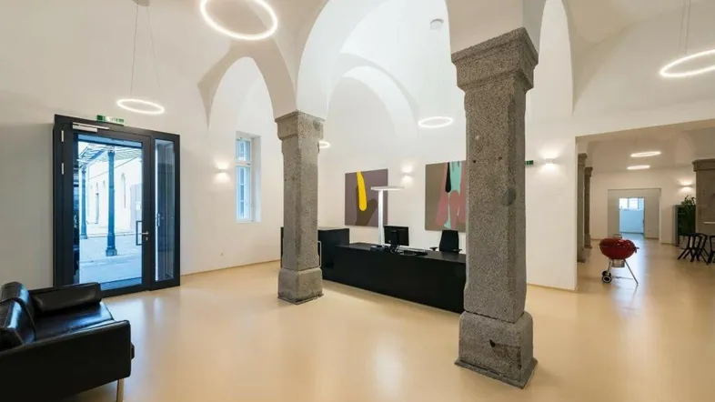 Geräumiger Empfangsbereich mit hohen Gewölbedecken, steinernen Säulen und modernen Ringlichtern.
