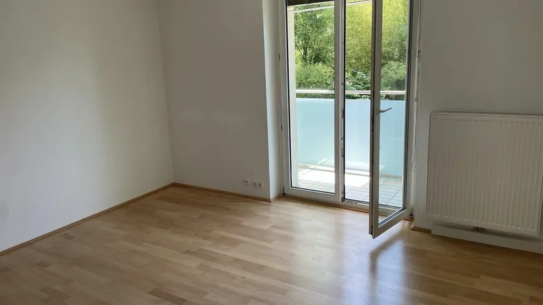 Helles Zimmer mit Holzboden und Zugang zu einem Balkon, ideal als Wohn- oder Schlafbereich.