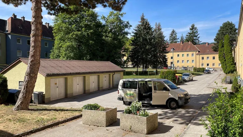 Außenansicht einer Wohnanlage mit Garagenreihe, Parkplätzen und viel Grün unter blauem Himmel.