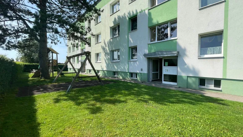Mehrfamilienhaus mit grün-weißer Fassade und Spielplatz im Gemeinschaftsgarten.