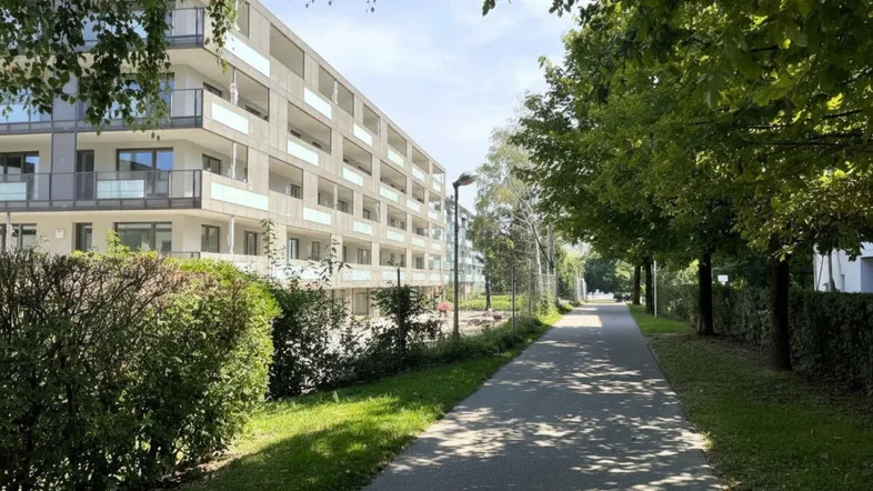 Moderne Wohnanlage mit Balkonen entlang eines grünen Spazierwegs an einem sonnigen Tag.