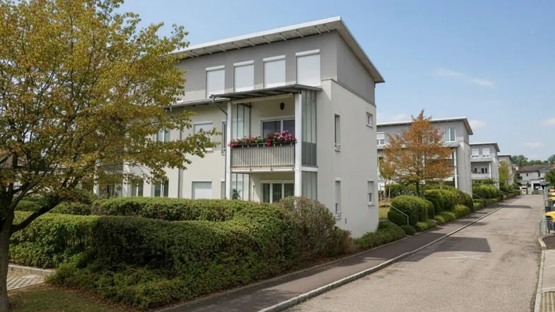 Modernes Mehrfamilienhaus mit Balkonen und gepflegter Heckenbepflanzung entlang der Straße.