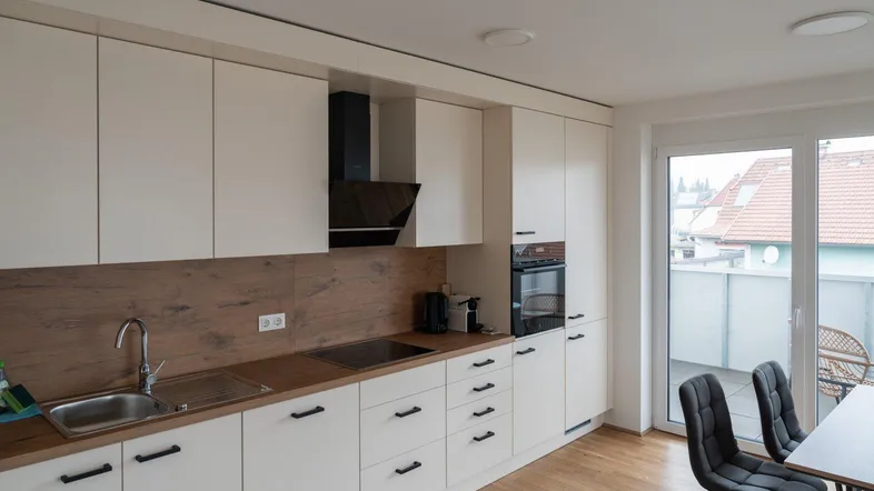 Moderne Küche mit weißen Schränken, Holzarbeitsplatte, integrierten Geräten und Zugang zum Balkon.