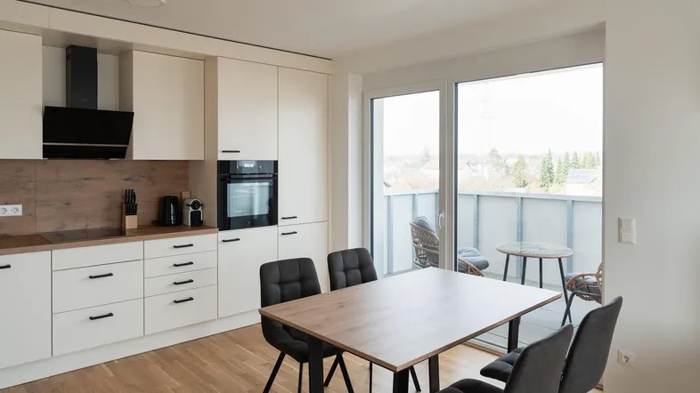 Moderne Küche mit weißen Schränken, Holzakzenten und Essbereich mit Zugang zum Balkon.