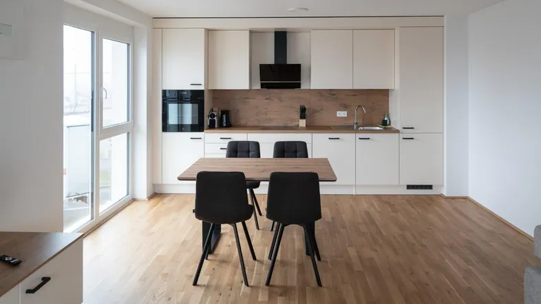 Moderne offene Küche mit integriertem Essbereich, Holzboden und Zugang zu einem Balkon.