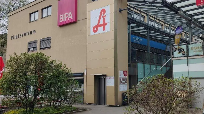 Außenansicht eines Vitalzentrums mit Apotheke und BIPA-Filiale, umgeben von Grünflächen.