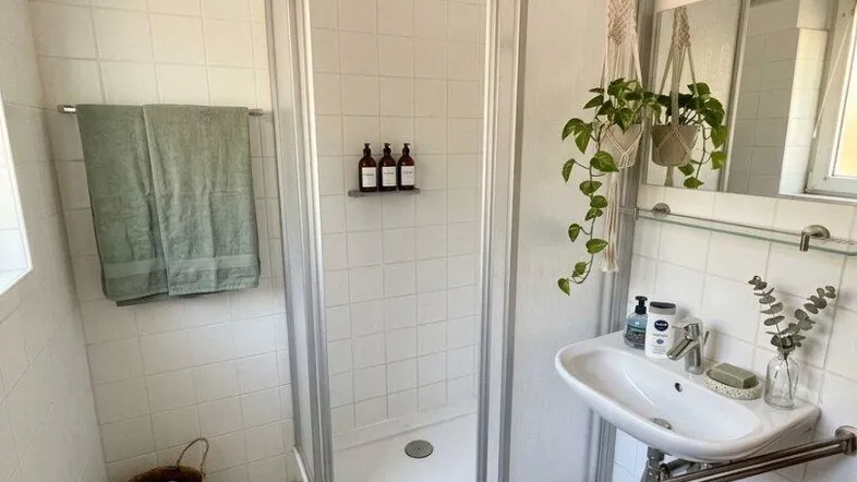 Helles Badezimmer mit Duschkabine, Waschbecken und weißen Fliesenboden.